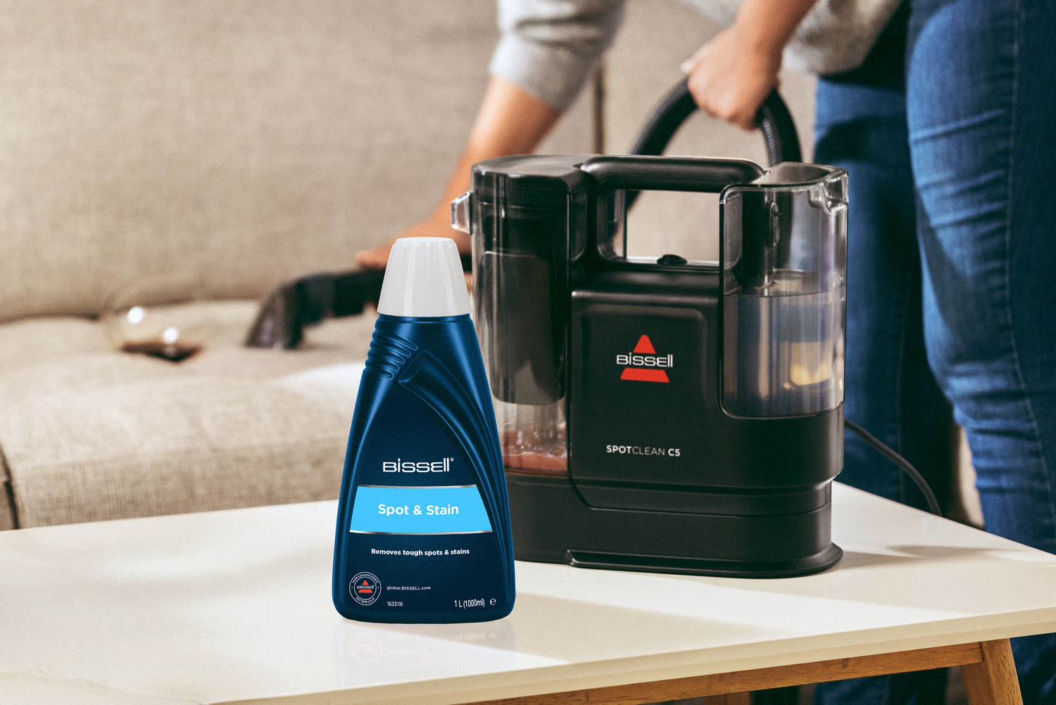 Botella de limpiador Bissell Spot & Stain y máquina SpotClean C5 sobre mesa.