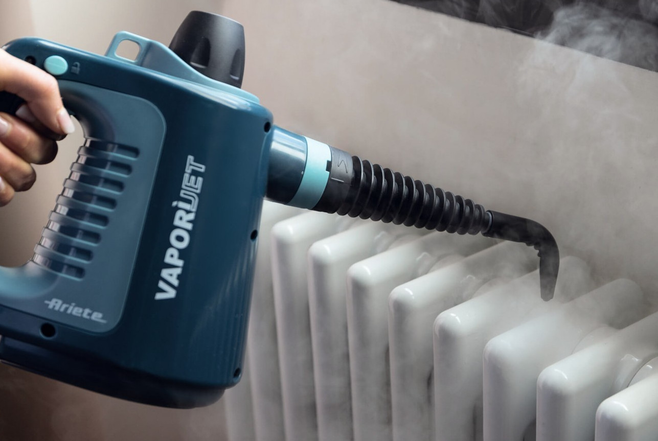 Turkusowy czyścik parowy z logo 'VaporJet' rozpyla parę na biały grzejnik.
