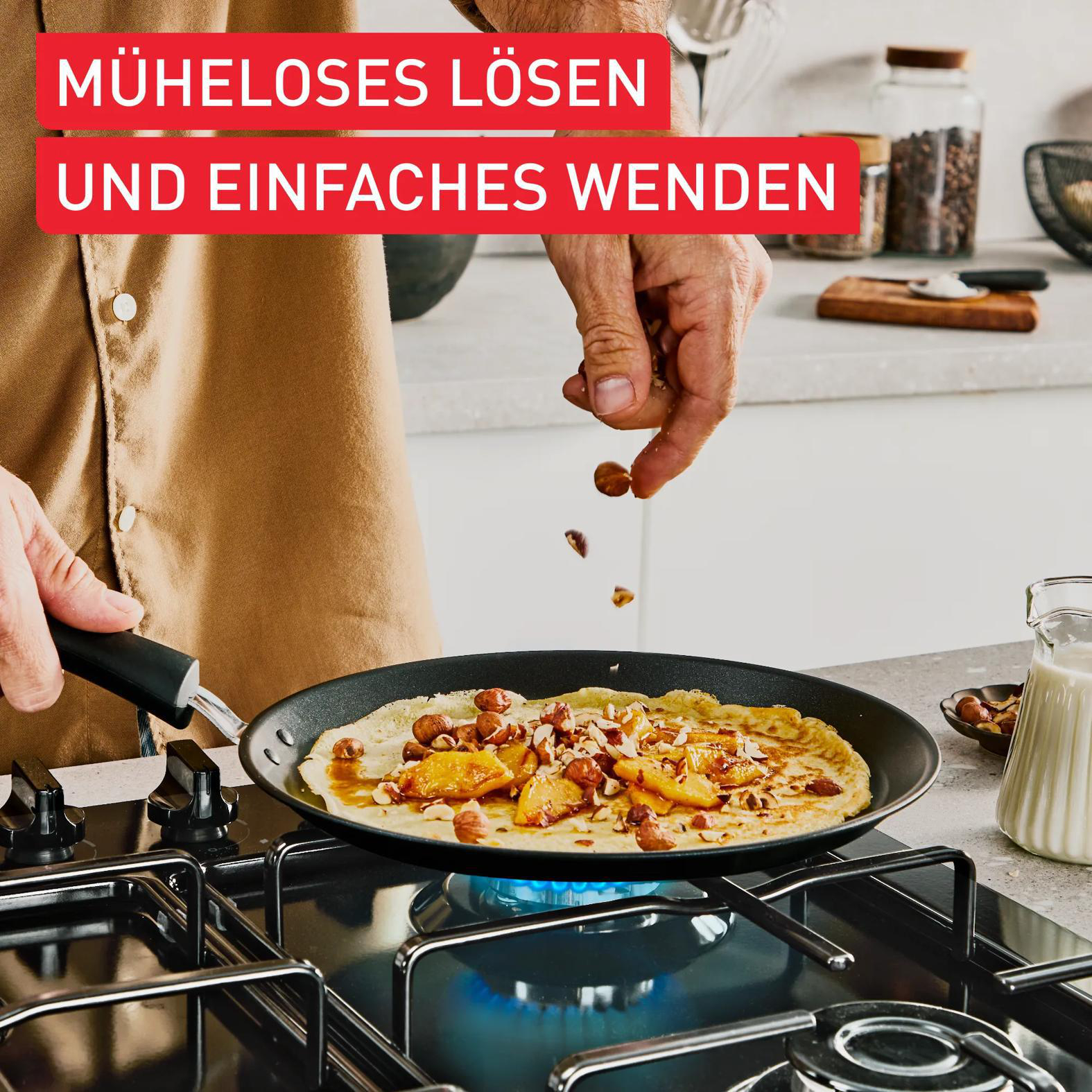 Ein Koch streut Nüsse auf einen Pfannkuchen in einer Pfanne auf einem Gasherd.