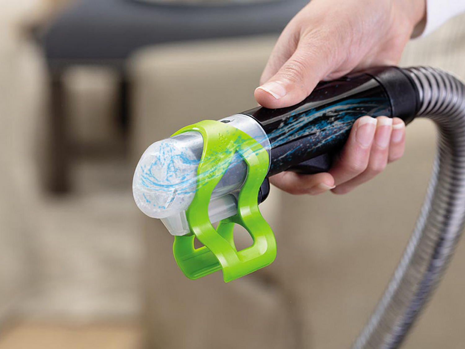 Mano sosteniendo tubo de aspiradora con accesorio verde y partículas azules.