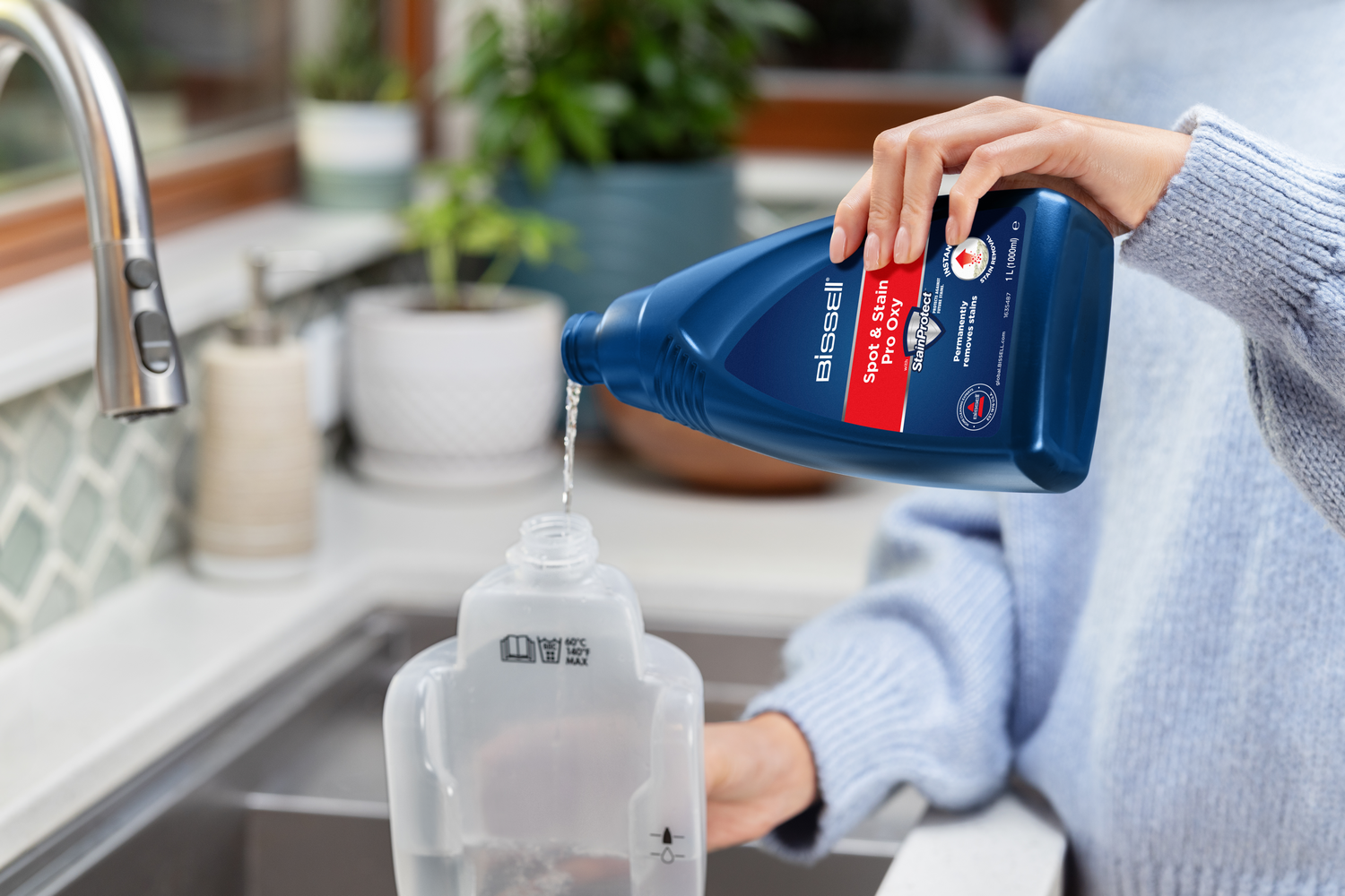 Una persona vierte Bissell Spot & Stain Pro Oxy de una botella azul en un recipiente transparente.