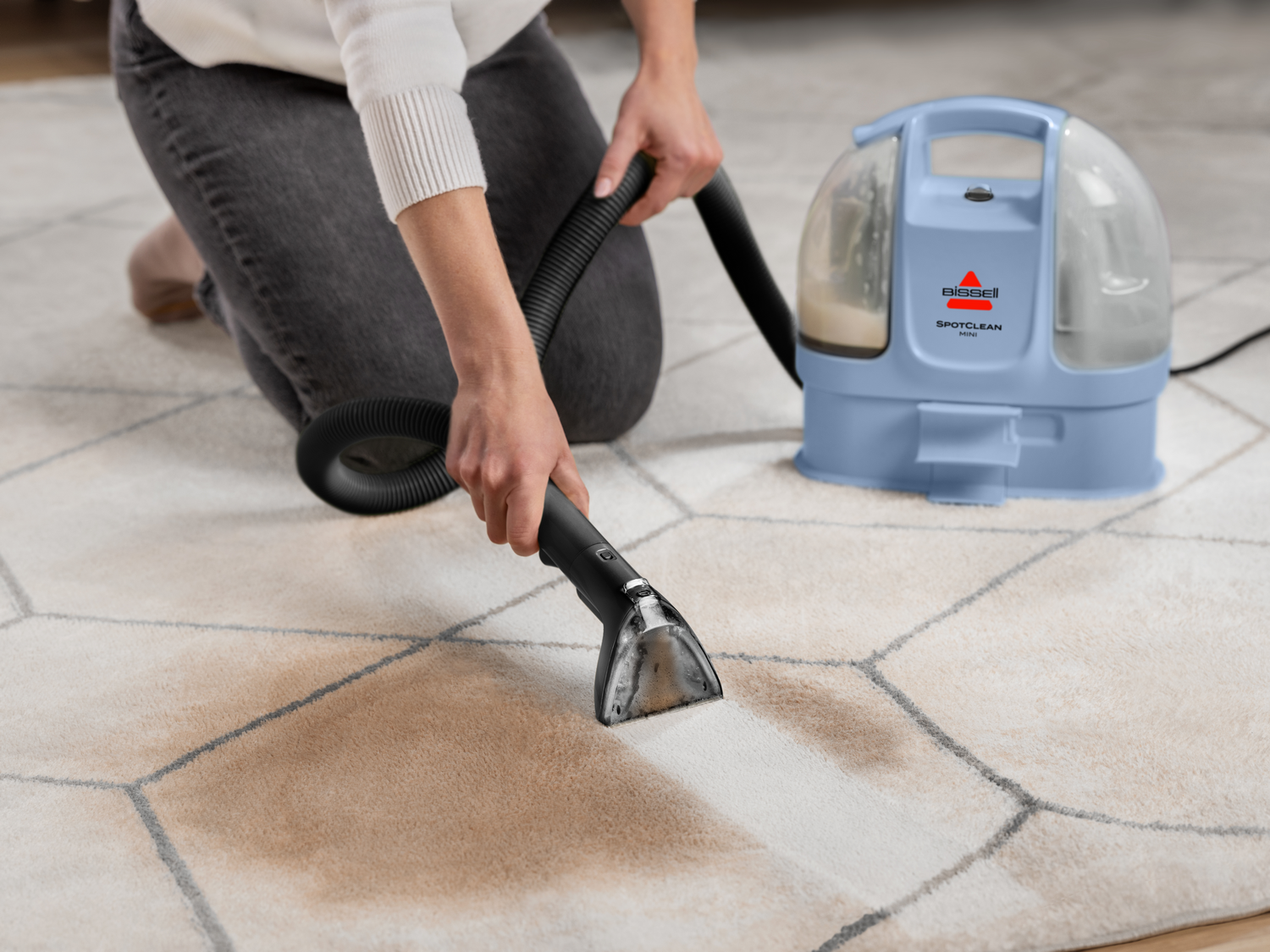 Persona limpiando alfombra con un dispositivo BISSELL SpotClean Mini azul.