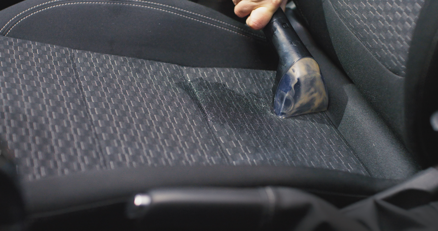 Una aspiradora de mano limpia un asiento oscuro de tapicería de coche.