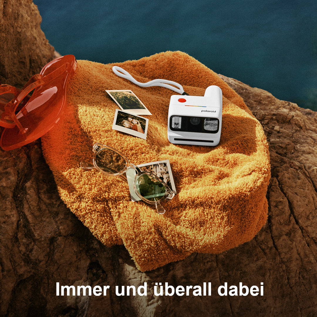 Orange Handtuch mit Polaroidkamera, Sonnenbrille, Flip-Flops und Fotos am Meer.