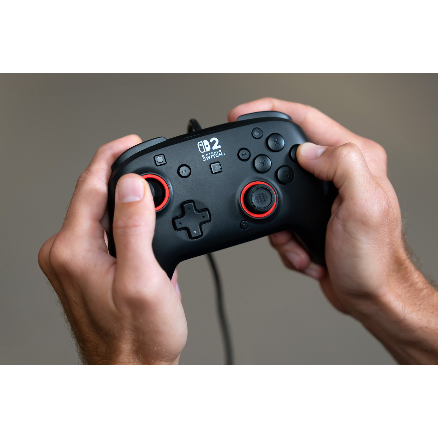 Hands holding a black Nintendo Switch controller with red accents.