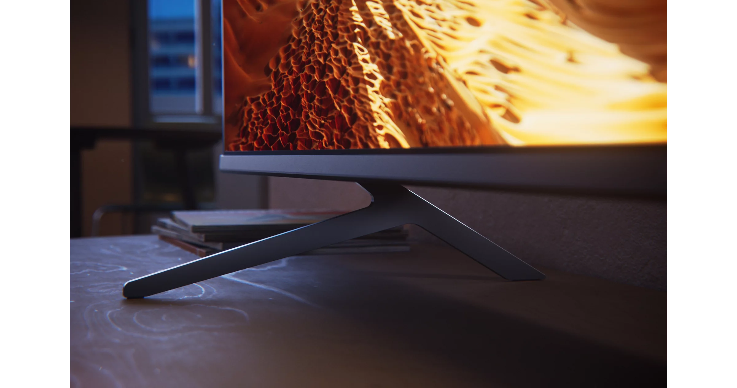 Ein moderner Fernsehbildschirm zeigt abstrakte orange-gelbe Muster. Der Fernseher steht auf einem dunklen Ständer auf einem Holztisch.
