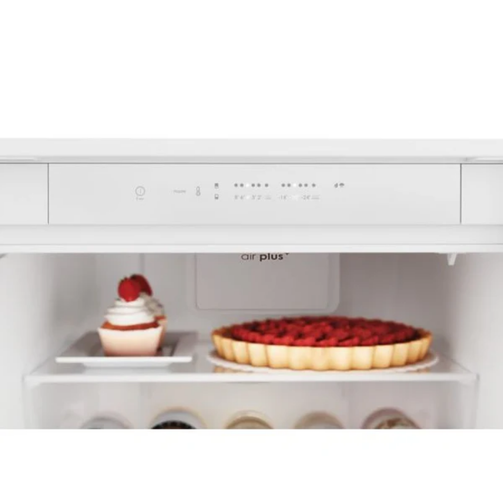 Un cupcake con fresas y una tarta de frutas sobre estantes dentro de un refrigerador blanco.