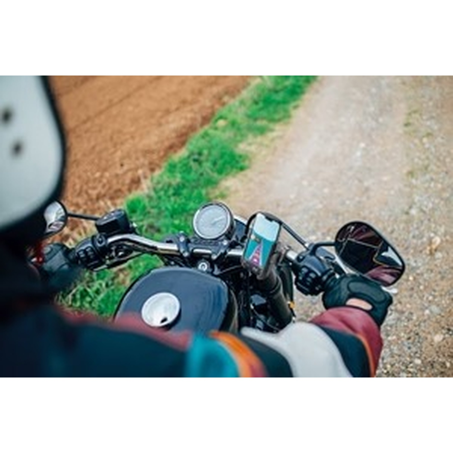Cavaliere su una moto, tiene il manubrio, con strada sterrata e campi.