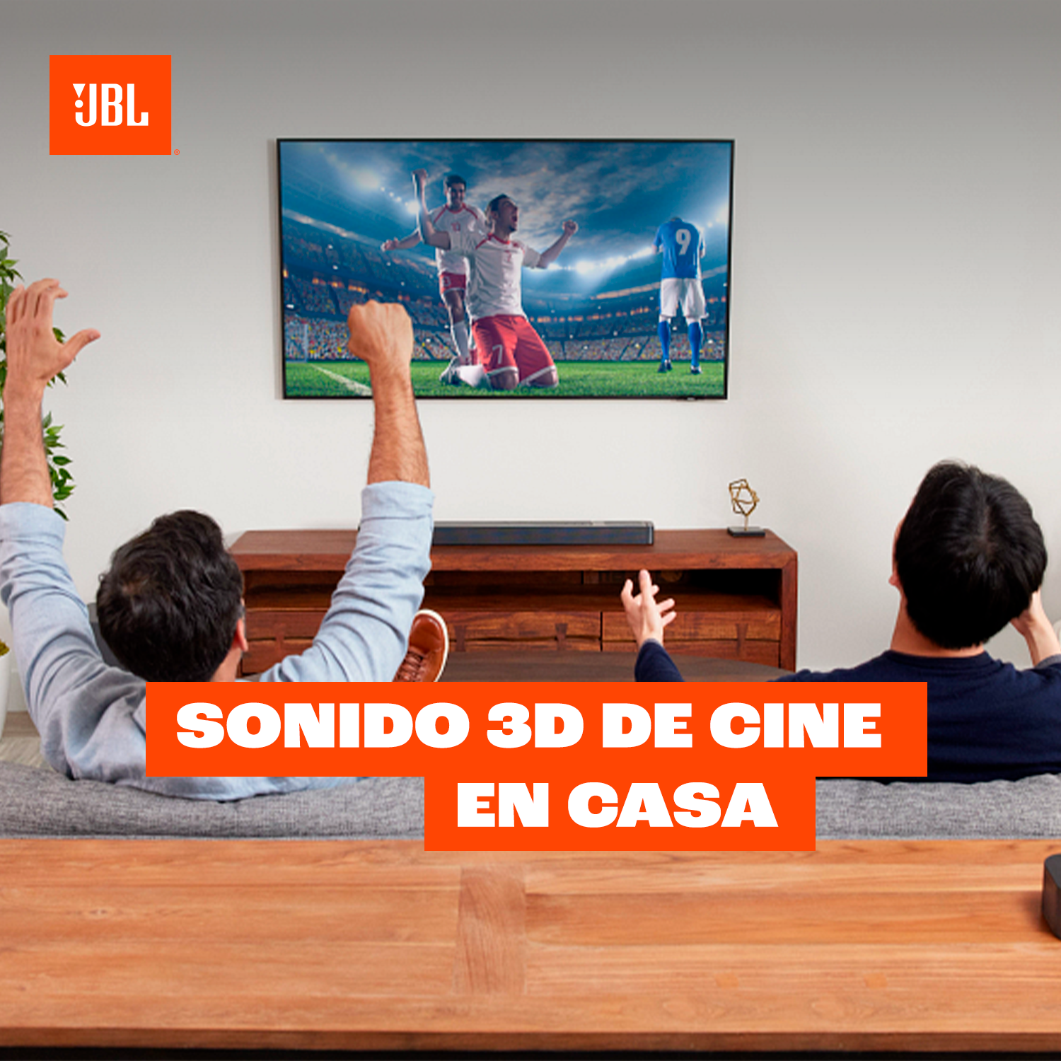 Dos hombres ven fútbol con emoción. Logo de JBL arriba.
