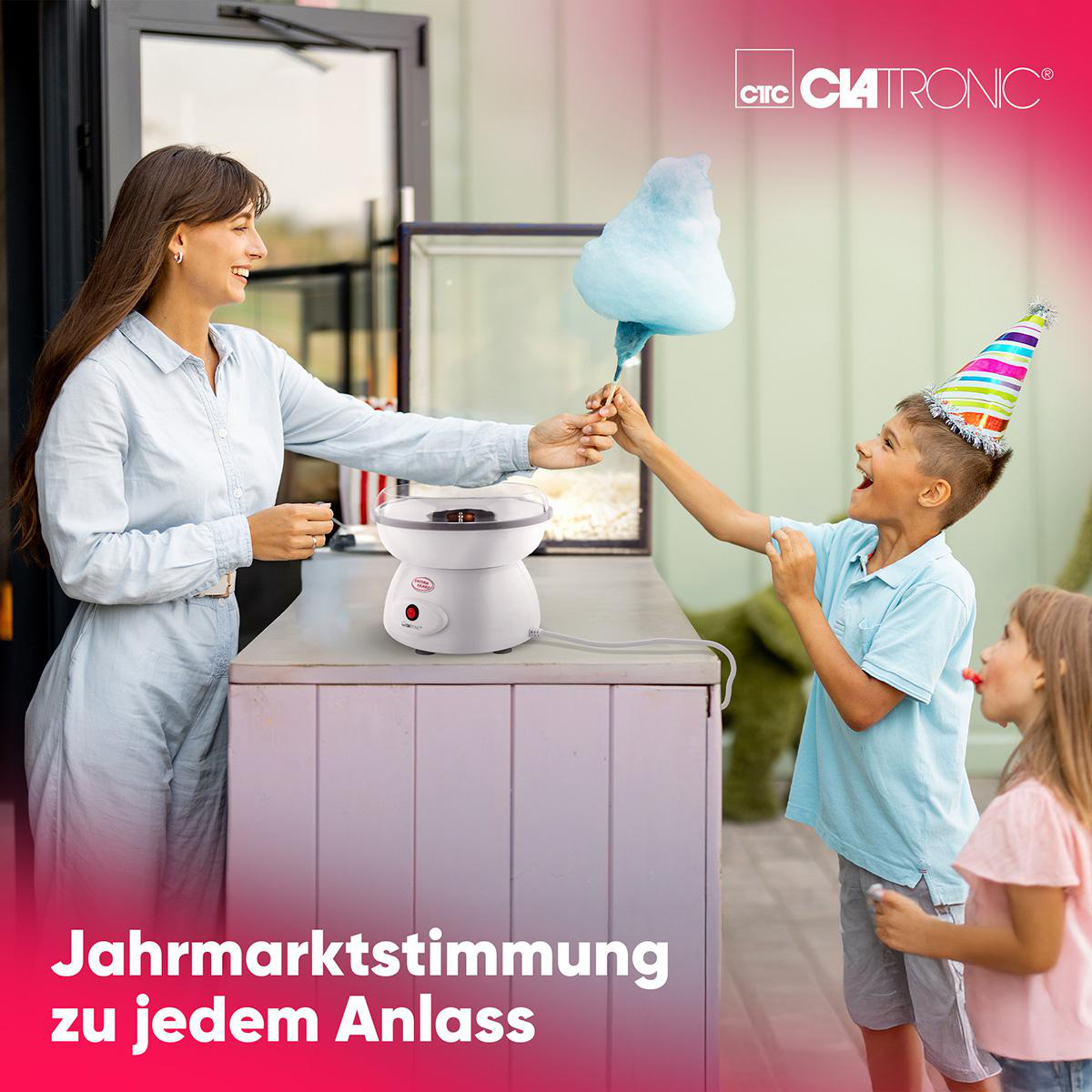 Eine Frau reicht einem Jungen Zuckerwatte von einer Maschine. Ein Mädchen schaut zu.