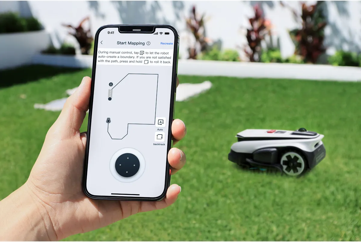 Eine Hand hält ein Smartphone mit einer Rasenmäher-App. Ein Mähroboter steht im Gras.