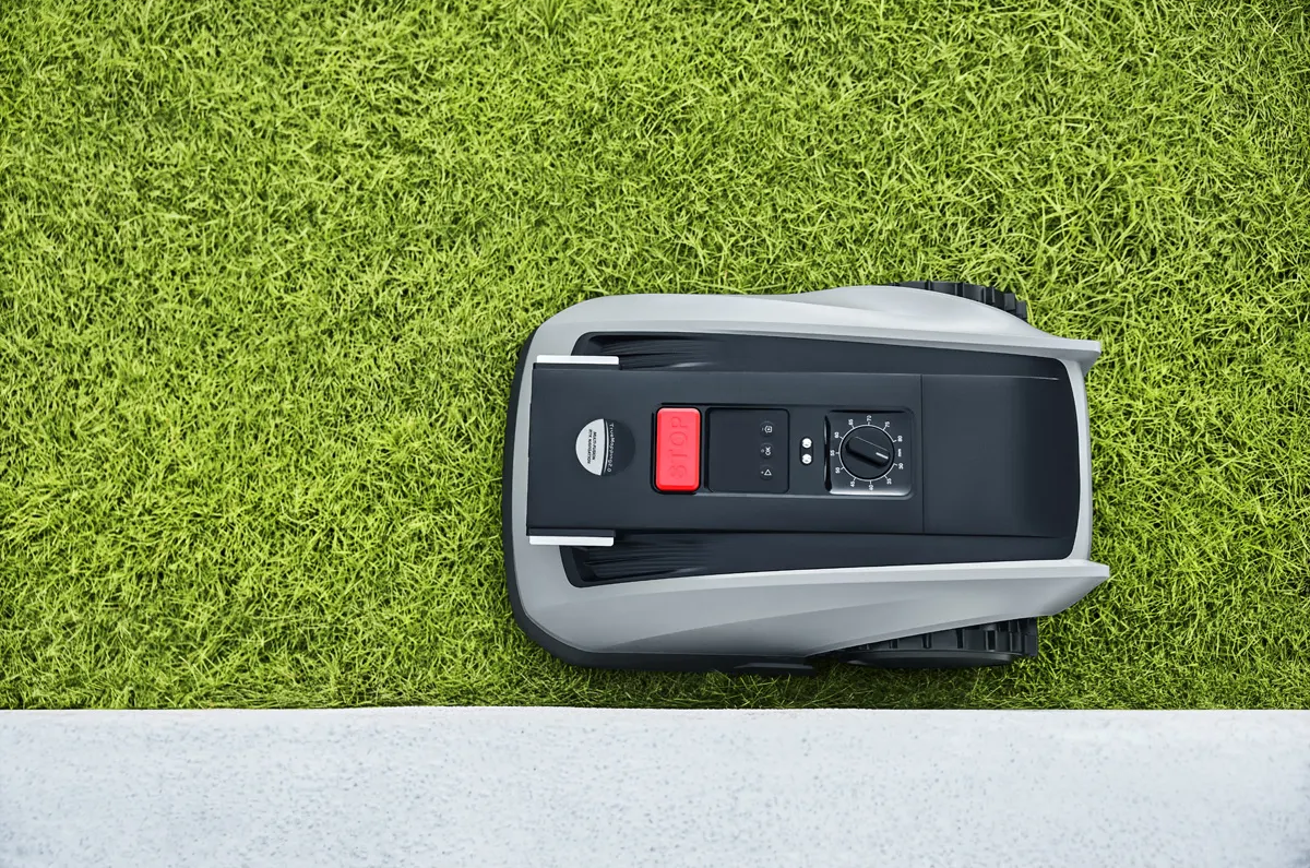 Ein Mähroboter mit rotem Stoppknopf auf einem grünen Rasen.