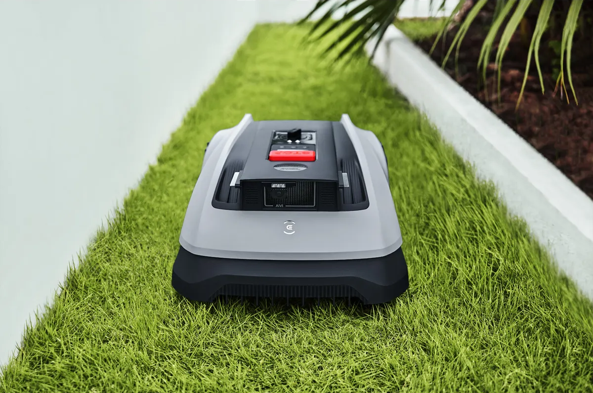 Ein grauer Mähroboter mit schwarzem Oberteil steht auf einem grünen Rasen.