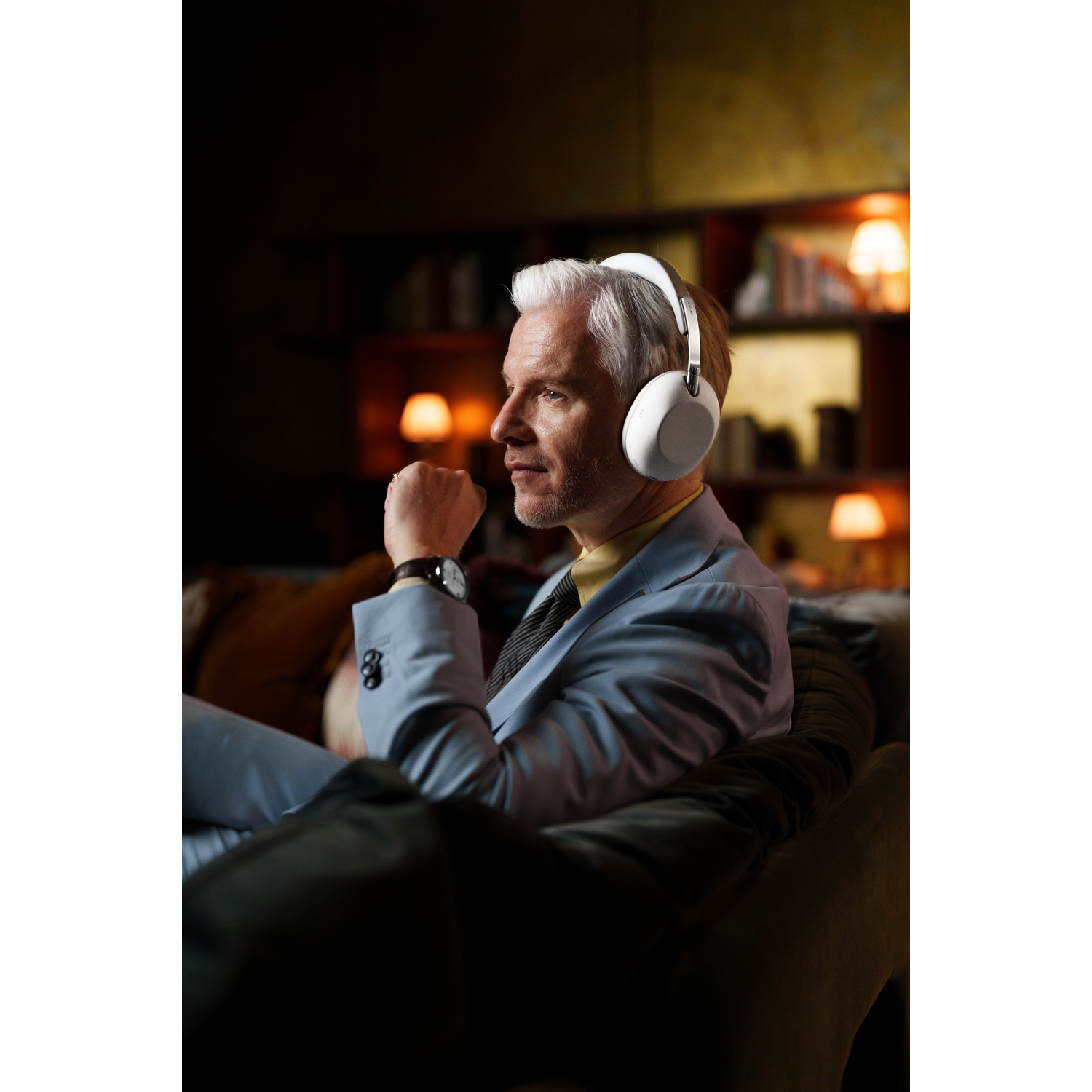 A man with white headphones sits on a sofa, looking to the right.