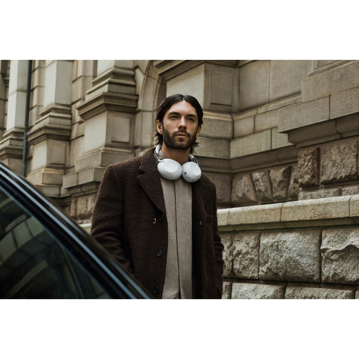 A man with headphones around his neck stands before a stone building.