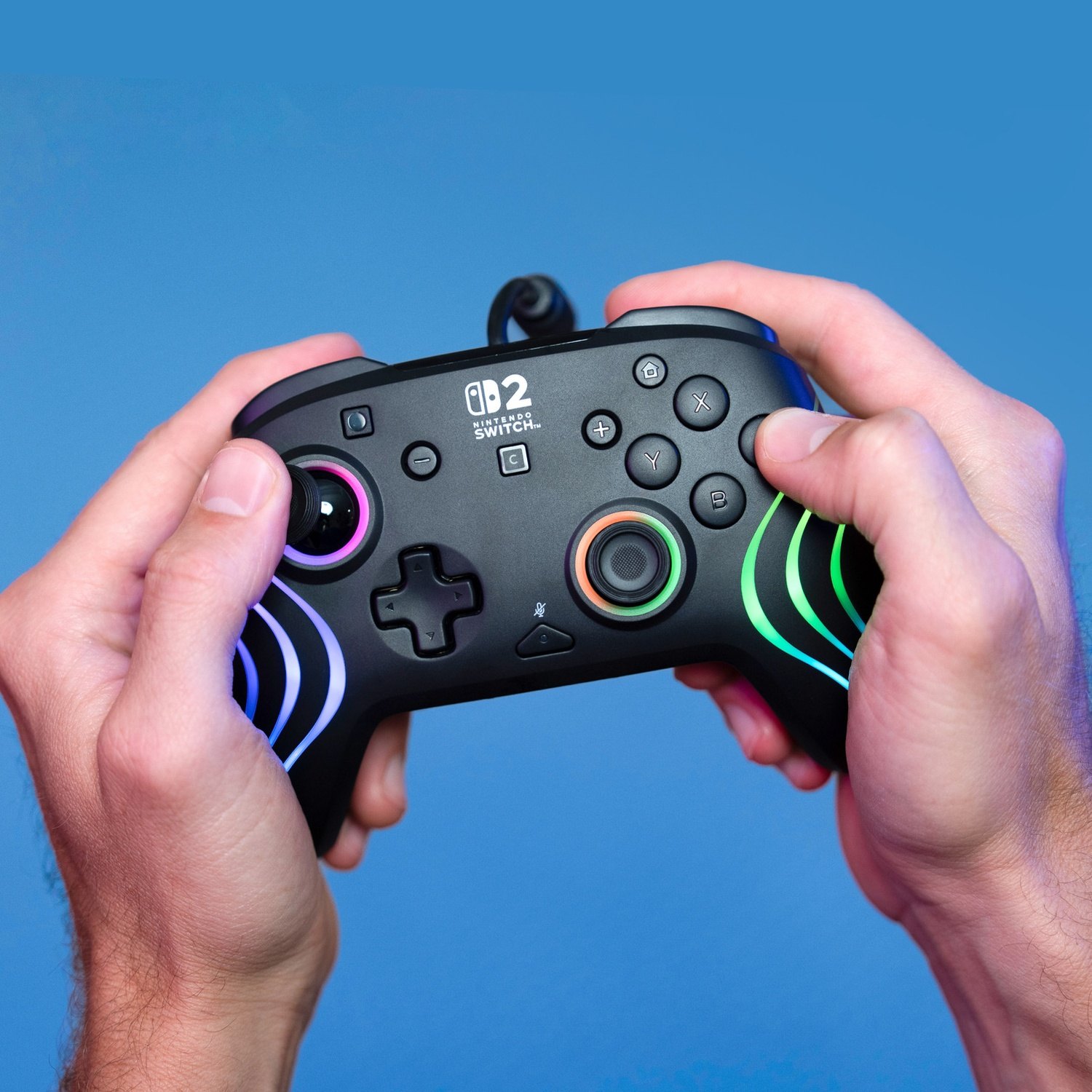 Mains tenant une manette noire Nintendo Switch avec des lumières colorées.
