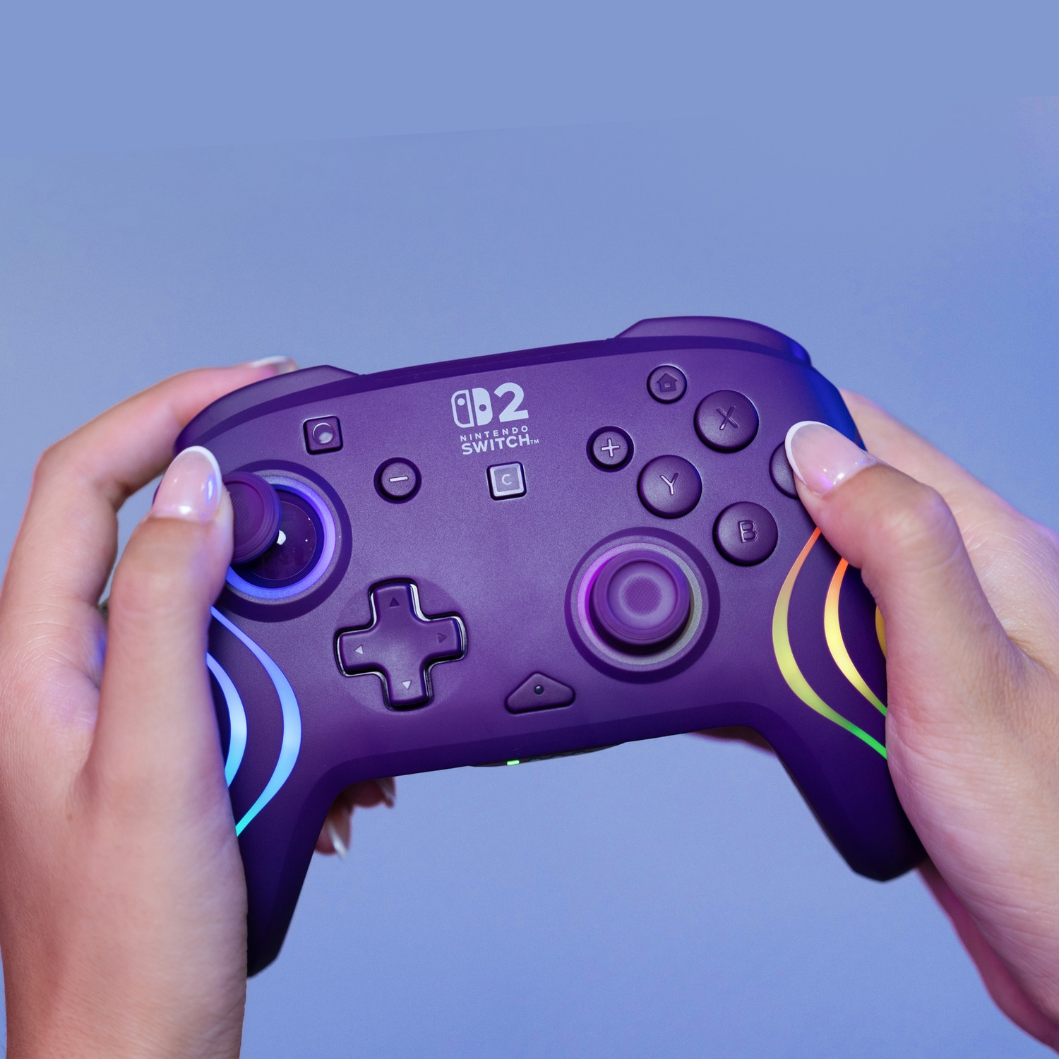 Des mains tiennent une manette violette Nintendo Switch avec des accents arc-en-ciel lumineux.