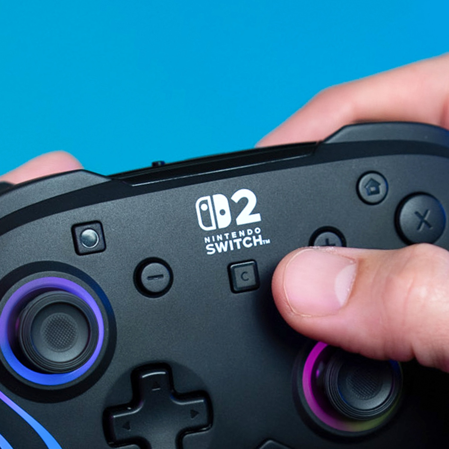 Gros plan d'une manette noire Nintendo Switch tenue par des mains sur fond bleu.