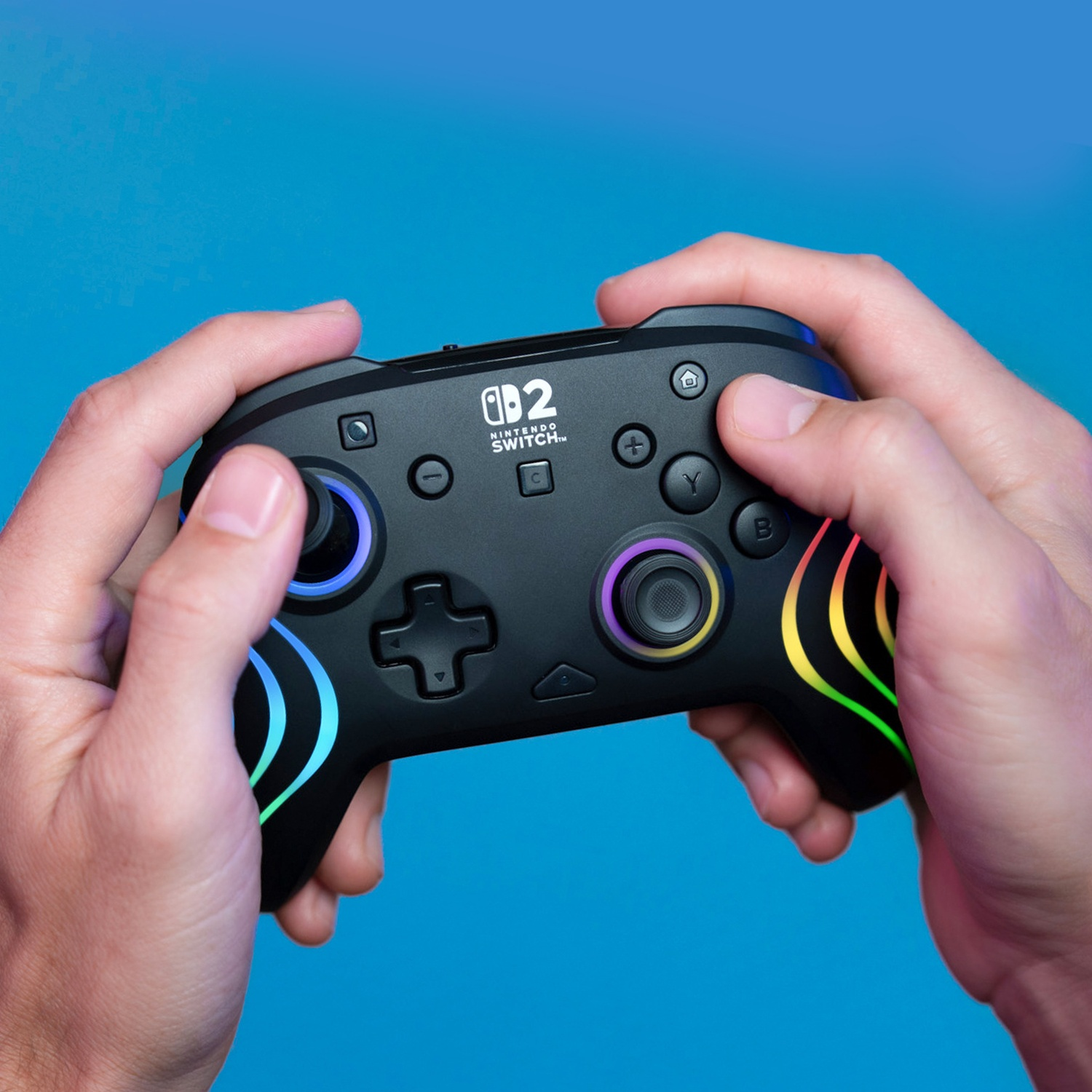 Des mains tiennent une manette noire Nintendo Switch avec des lumières colorées.
