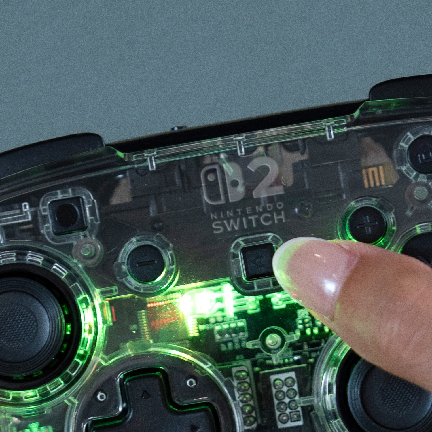 Manette Nintendo Switch transparente avec éclairage vert, doigt appuyant sur un bouton.