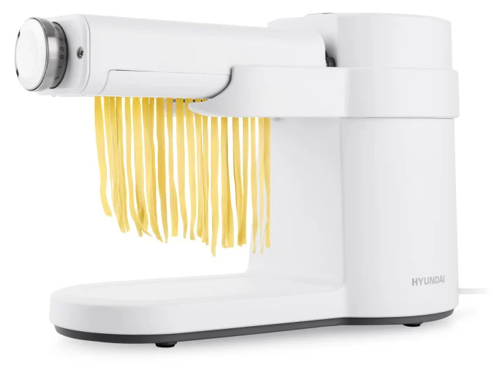 Egy fehér tésztagép friss, sárga fettuccine tésztát extrudál.