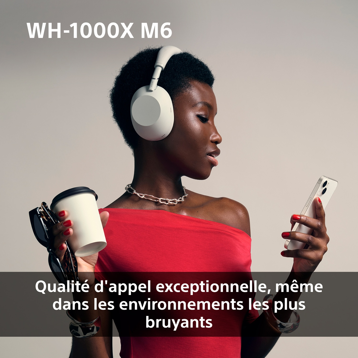 Une femme avec un casque tient un téléphone et une tasse. Elle porte un haut rouge.