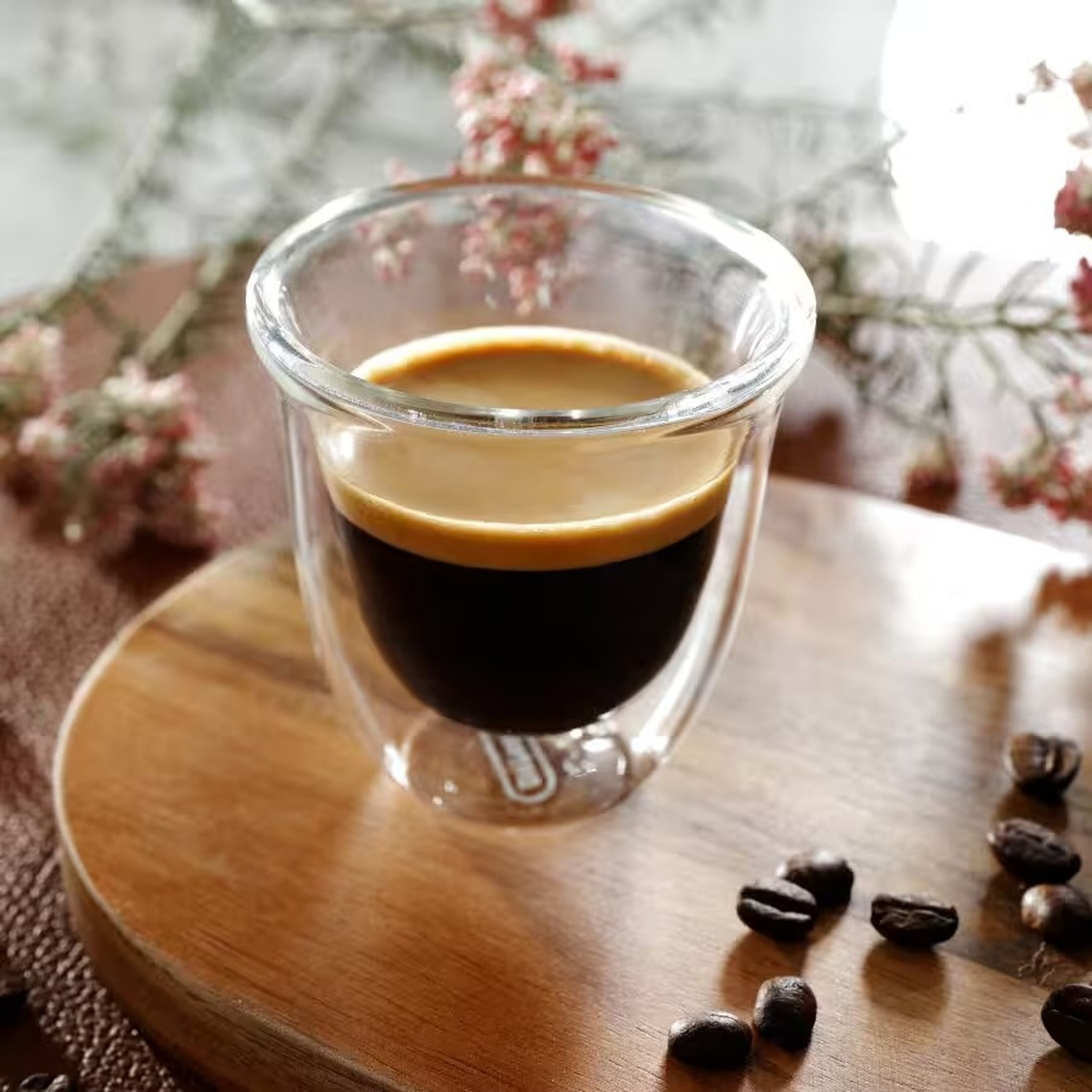 Un bicchiere di espresso con crema su tagliere di legno, circondato da chicchi.
