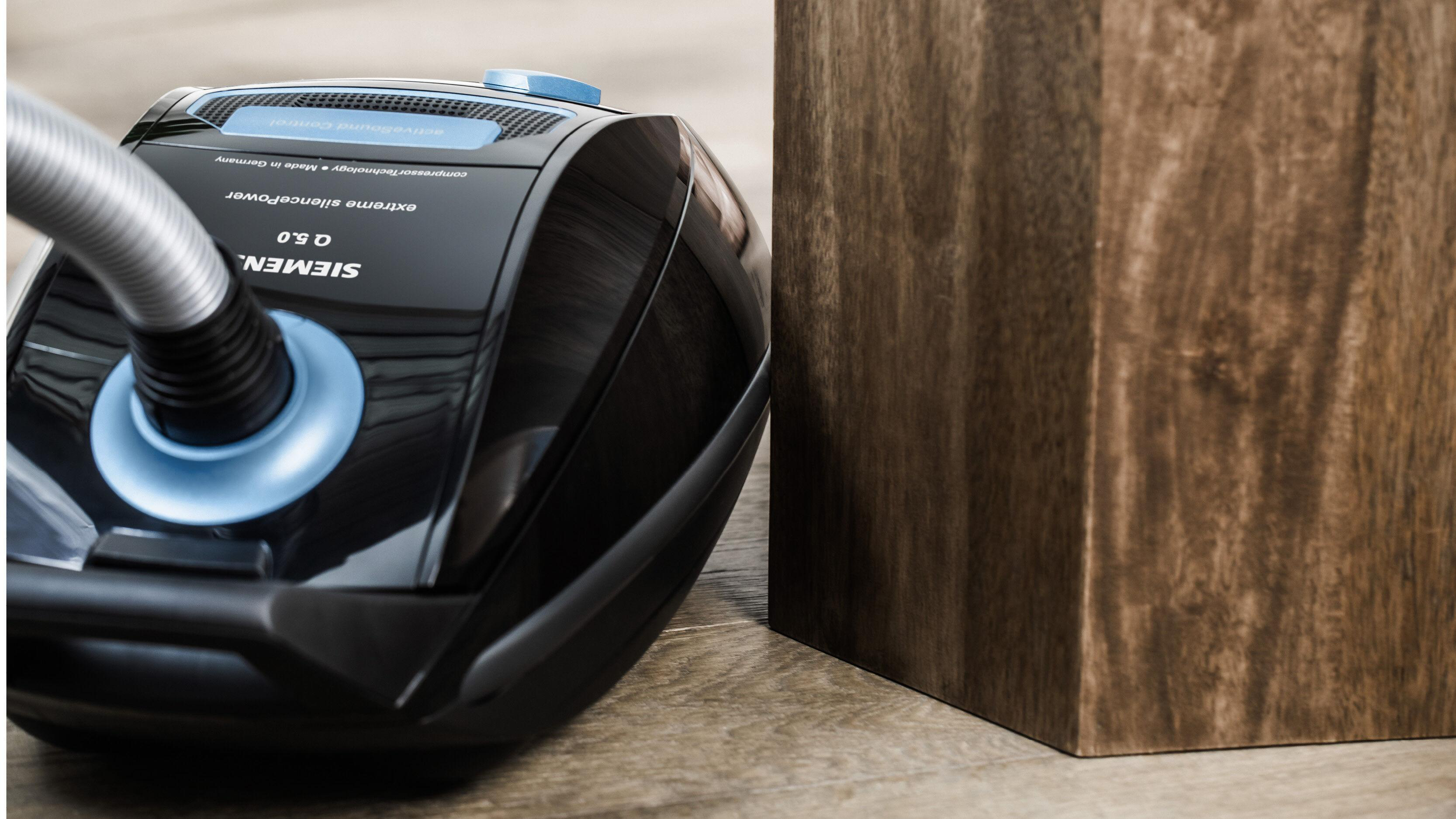 Ein schwarzer Siemens Staubsauger mit blauem Schlauchanschluss neben einem Holzwürfel.