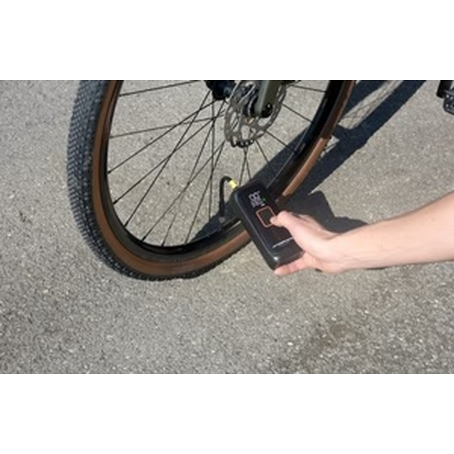 Una mano tiene un gonfiatore per pneumatici vicino alla ruota di una bicicletta sull'asfalto.