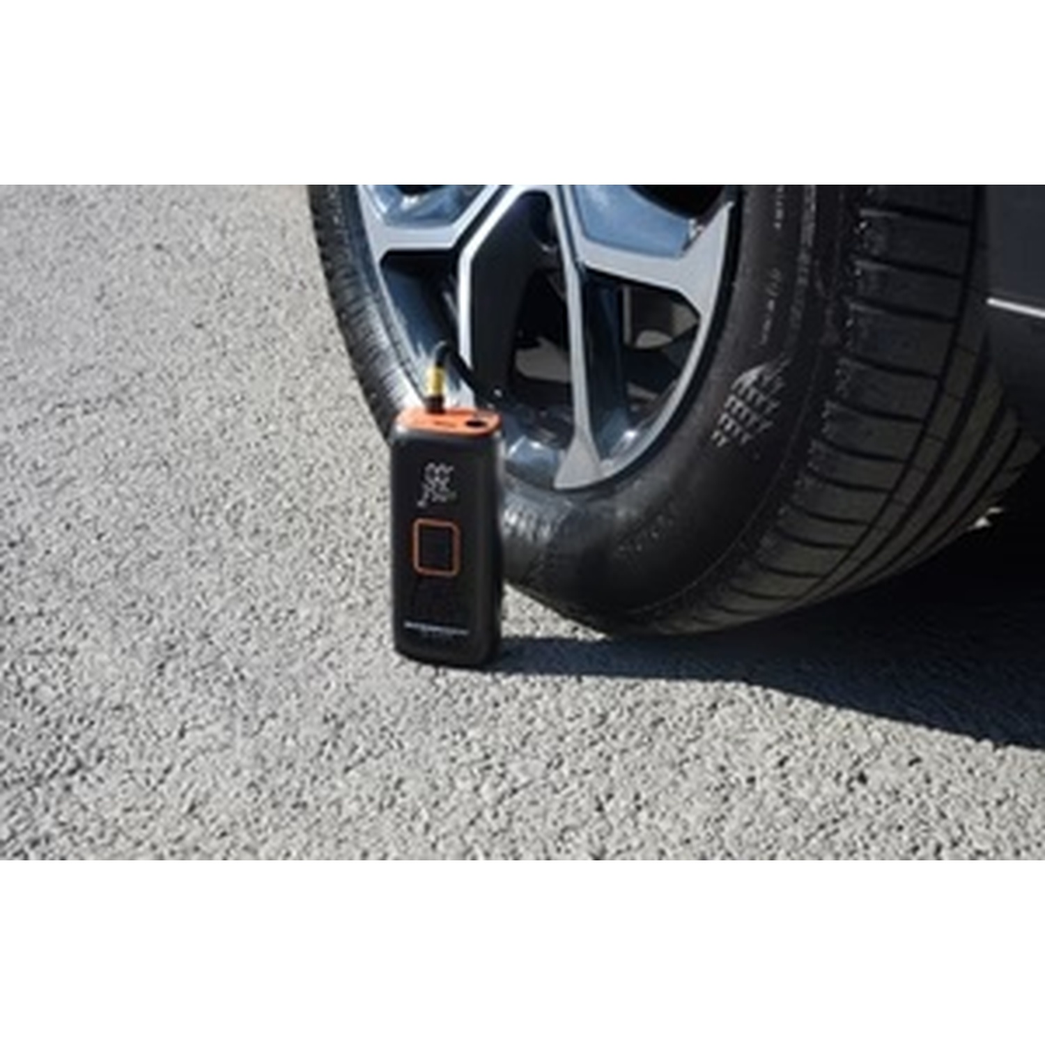 Un compressore d'aria portatile accanto a uno pneumatico per auto sull'asfalto.