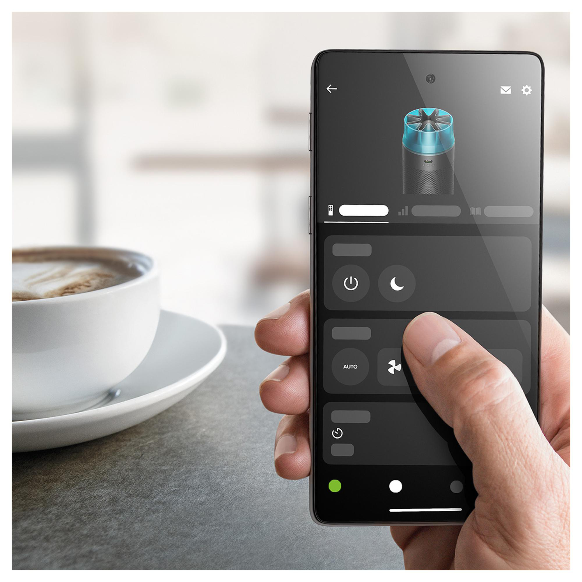Eine Hand hält ein Smartphone mit einer App, die einen Lüfter steuert. Daneben steht eine Kaffeetasse.