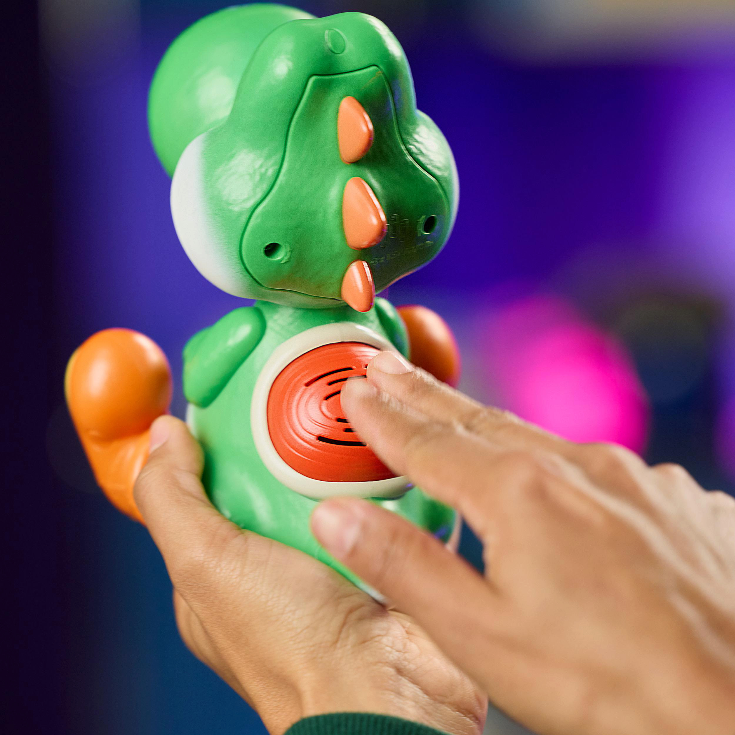 Eine Hand drückt auf einen grünen Spielzeugdino mit orangefarbenen Akzenten.