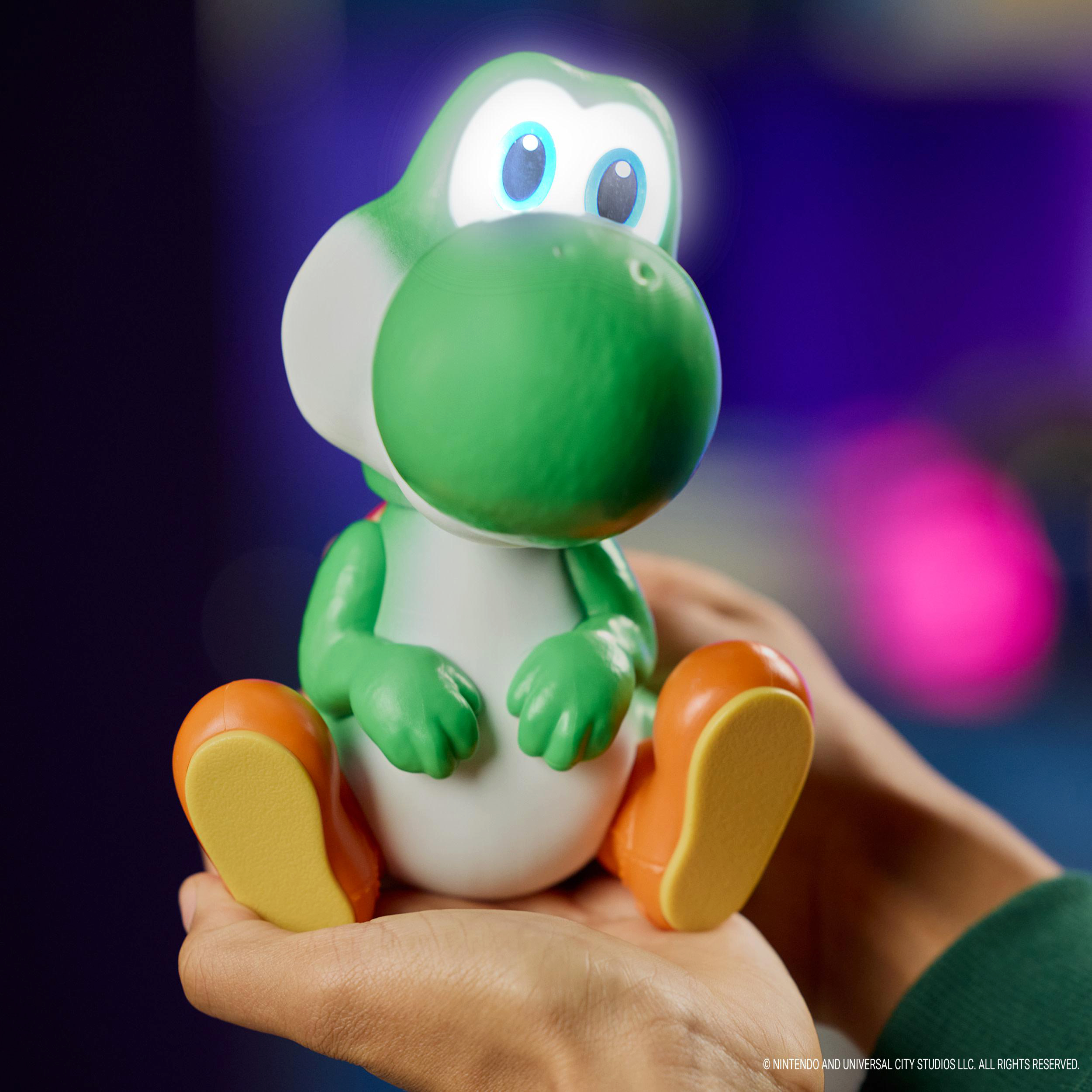 Eine grüne Yoshi-Figur sitzt in Händen. Der Hintergrund ist unscharf.