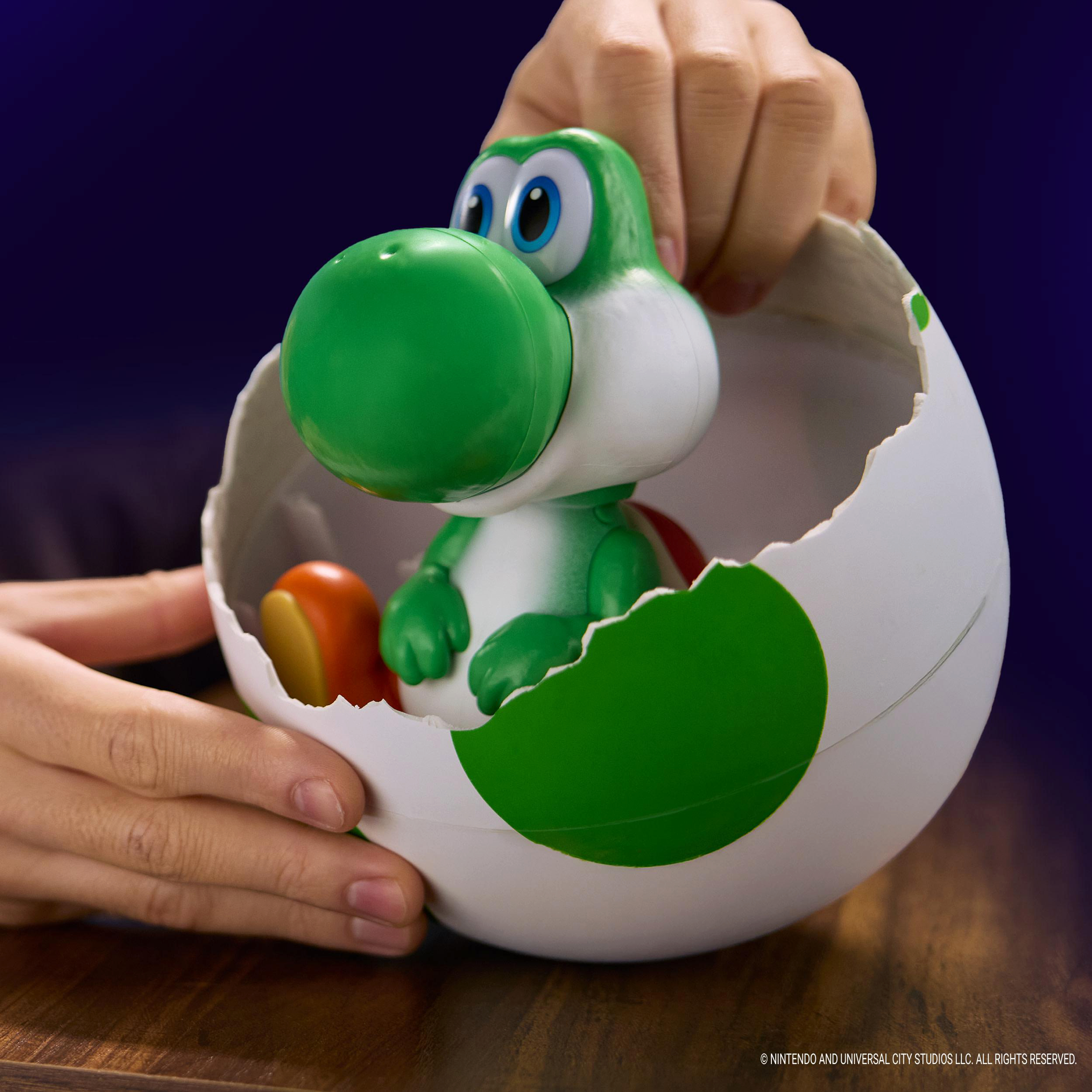 Eine grüne Yoshi-Figur schaut aus einem zerbrochenen weißen Ei auf einem Holztisch.