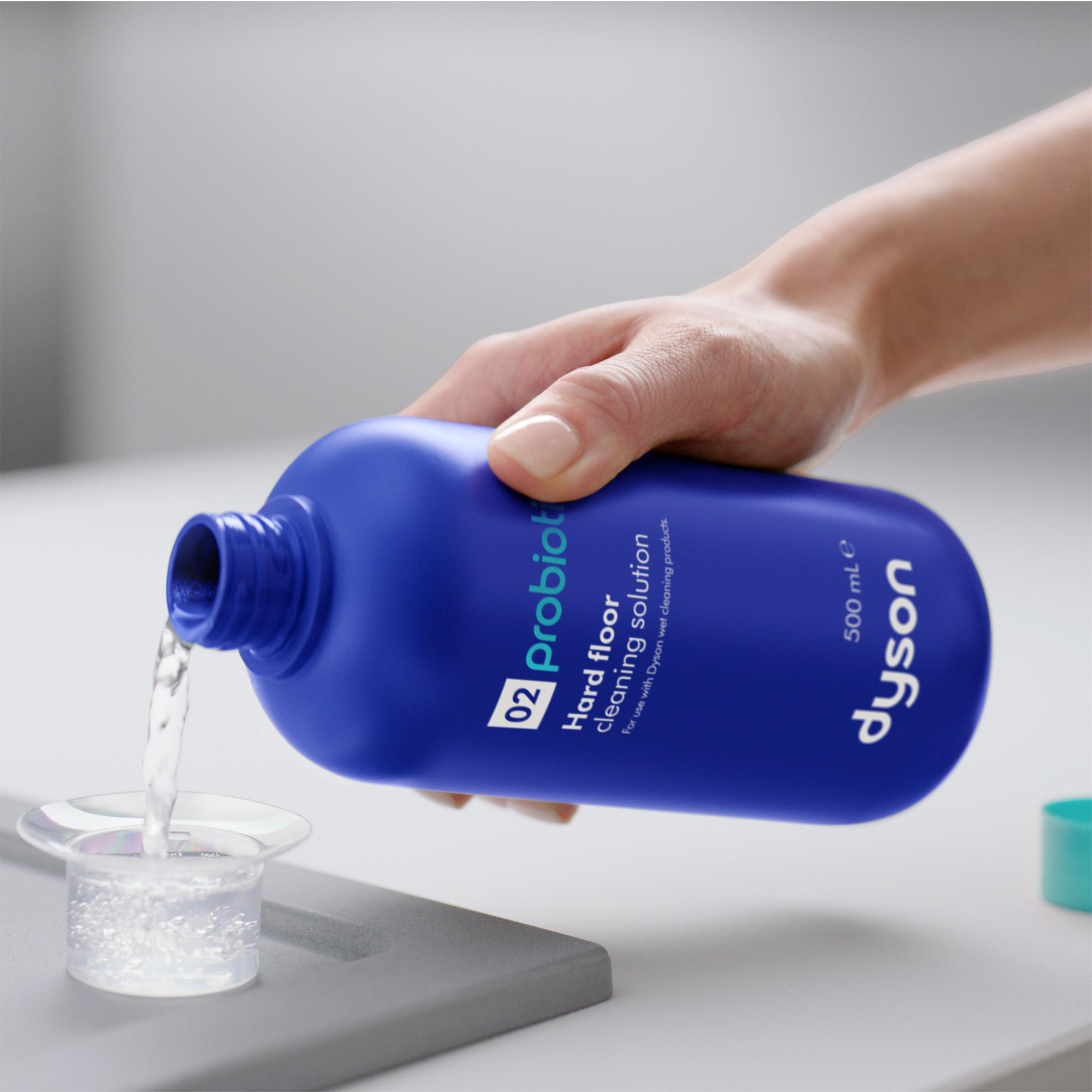 Eine Hand gießt blaue Dyson-Reinigungslösung in einen kleinen durchsichtigen Messbecher.
