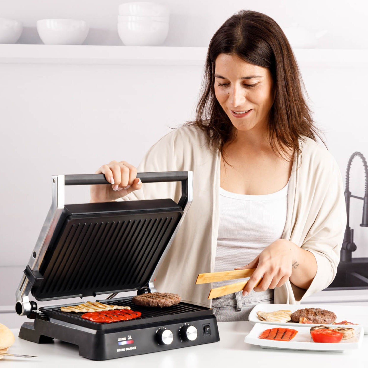 Mujer asando hamburguesas y pimientos en una parrilla de mesa.