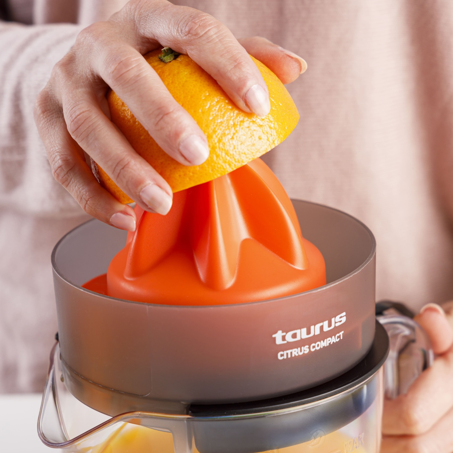 Una mano exprime una naranja en un exprimidor de cítricos naranja. Se ve jugo.
