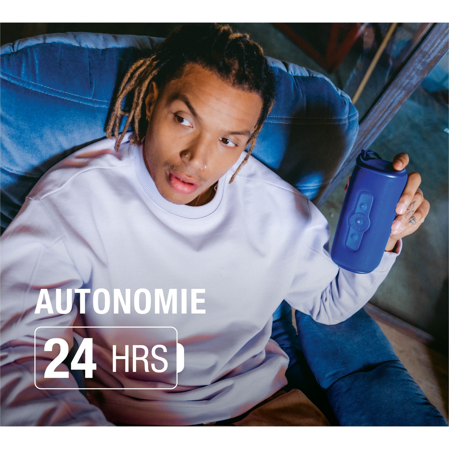 Homme aux dreadlocks tient enceinte bleue dans fauteuil, 24h d'autonomie.