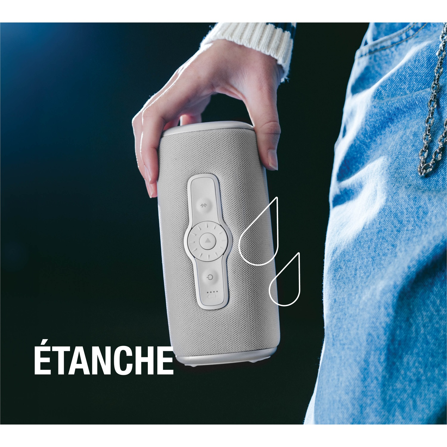 Une main tient un haut-parleur gris étanche contre du tissu en jean.