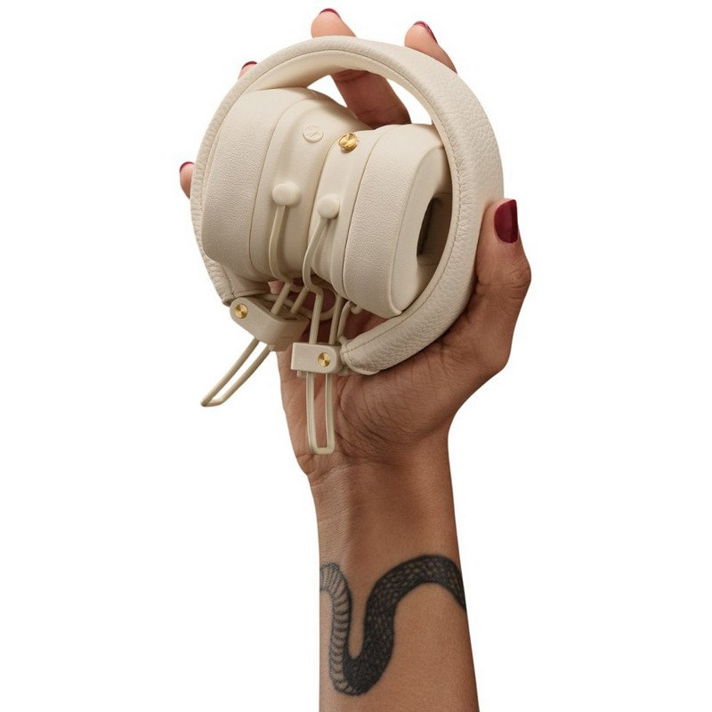 Una mano sostiene auriculares color crema con un tatuaje de serpiente en el antebrazo.
