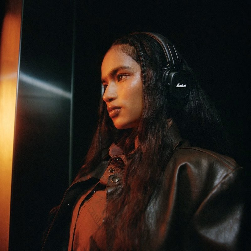 Una mujer de pelo largo y oscuro lleva auriculares negros y una chaqueta marrón.