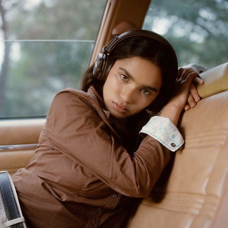 Una joven con auriculares se sienta en un coche, luciendo pensativa.