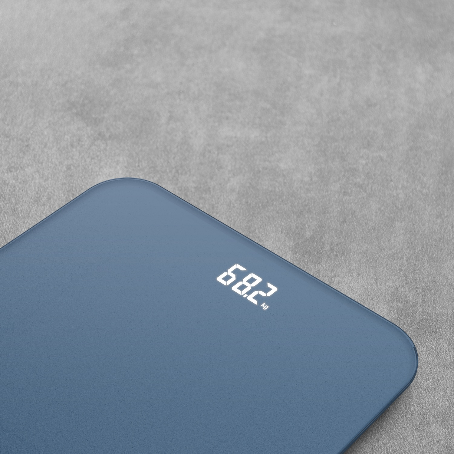 Une balance numérique bleue affiche 68,2 kg sur un fond gris.