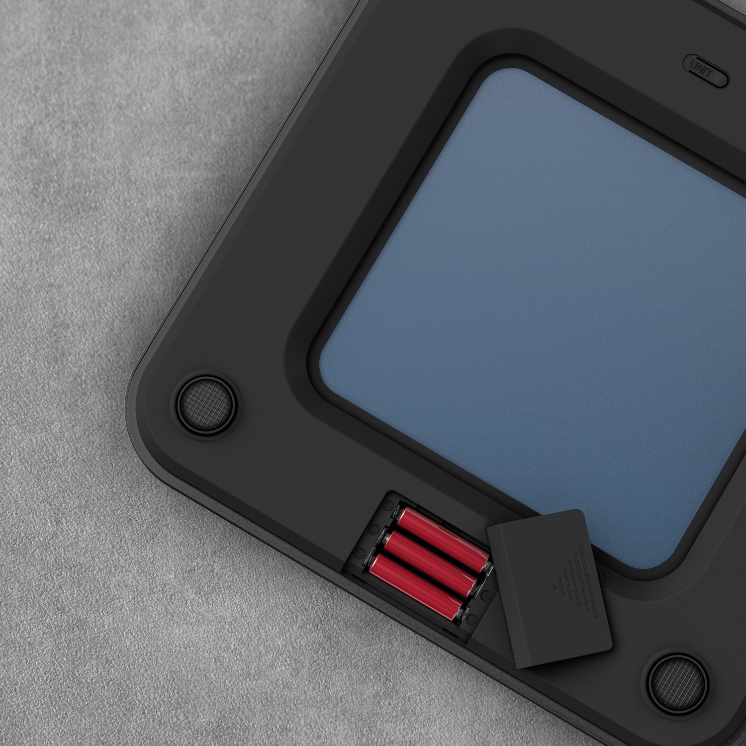 Appareil noir avec écran bleu et compartiment batterie ouvert avec trois piles rouges.