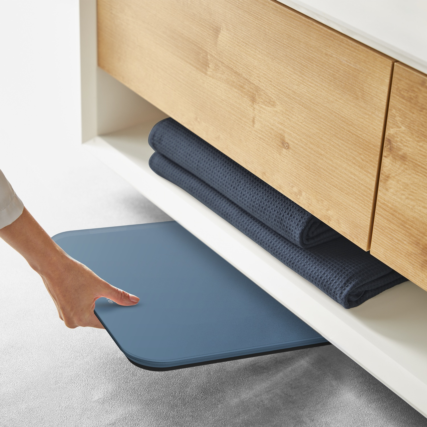 Une main retire un tapis bleu sous un meuble en bois avec des serviettes bleu foncé.
