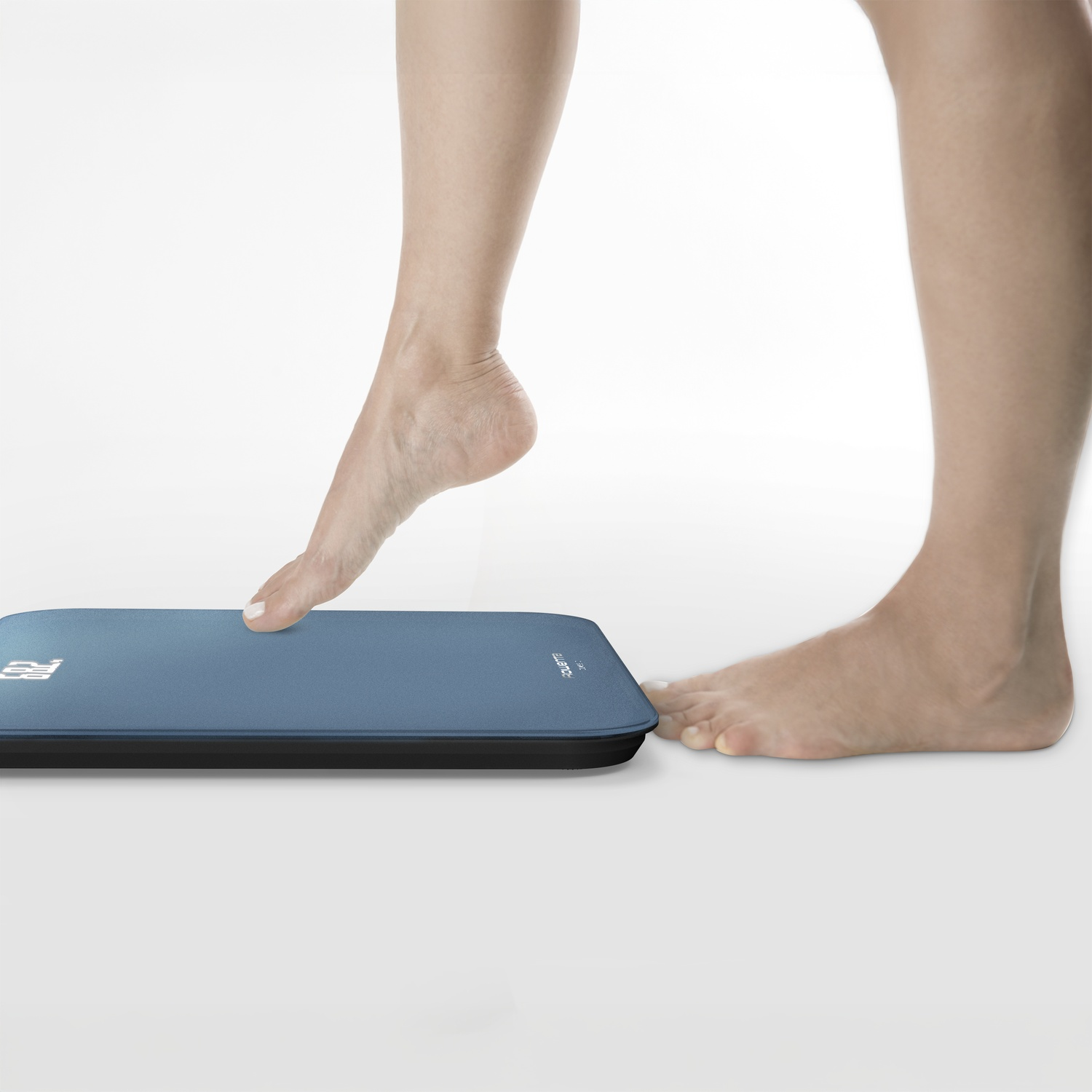 Une personne monte sur une balance numérique. Pieds sur la balance. Fond blanc.