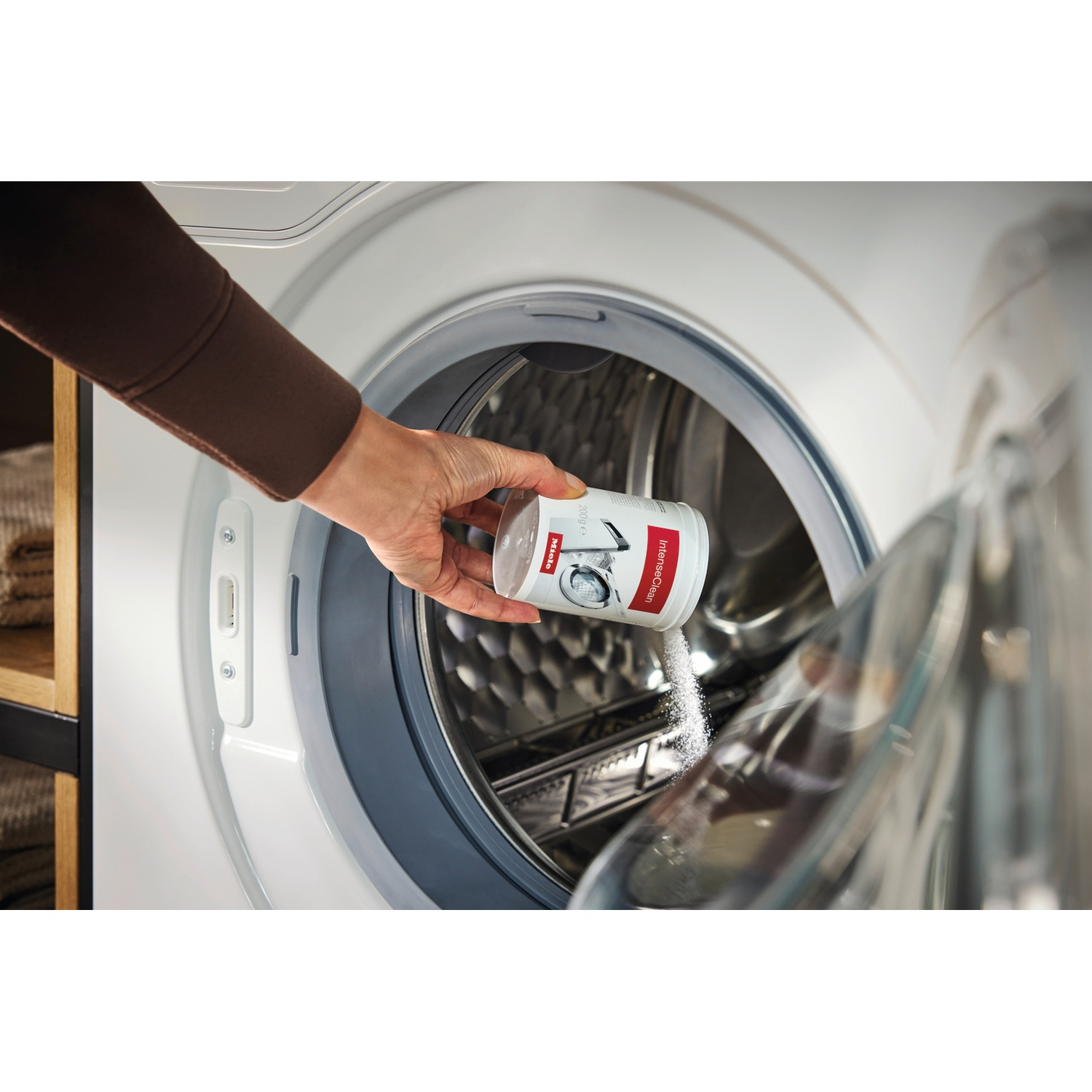 Een hand giet poeder uit een Miele reiniger in de trommel van een wasmachine.