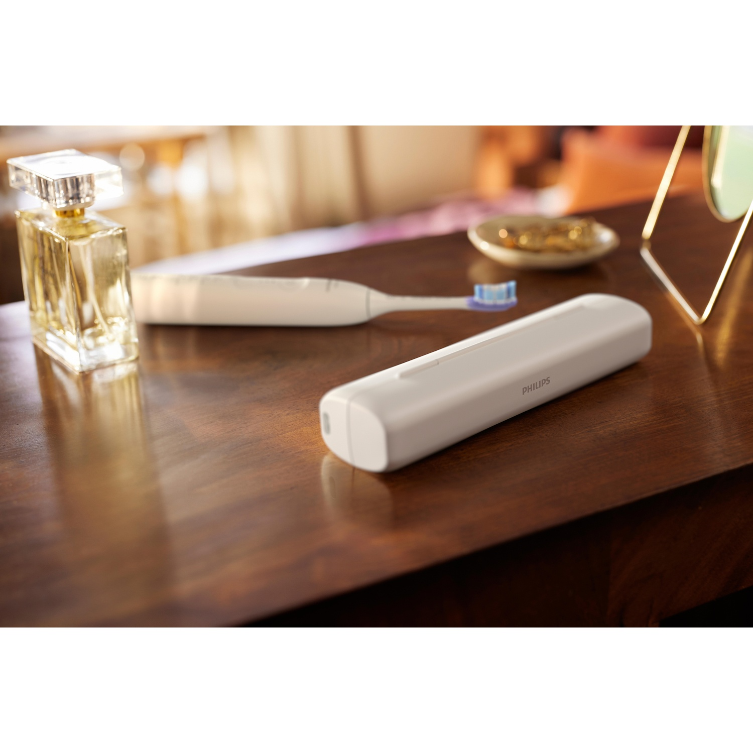 Un flacone di profumo, uno spazzolino bianco e un caricabatterie Philips su un tavolo di legno.