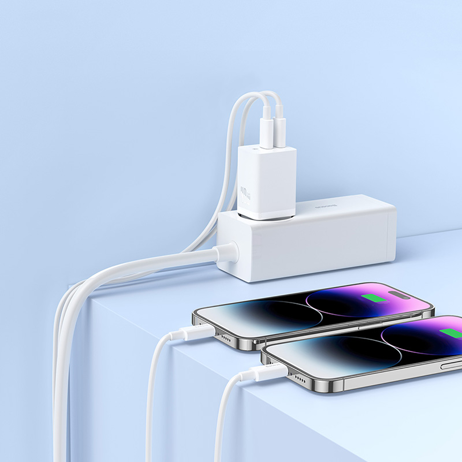 Dos smartphones cargando desde un adaptador de corriente y ladrillo blanco sobre superficie azul.