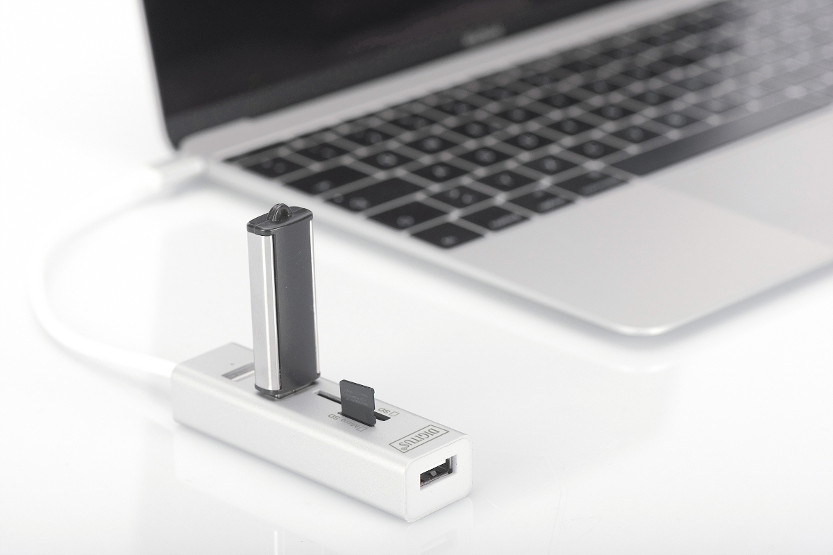Ein silberner USB-Hub mit eingestecktem USB-Stick und einer SD-Karte, neben einem Laptop.